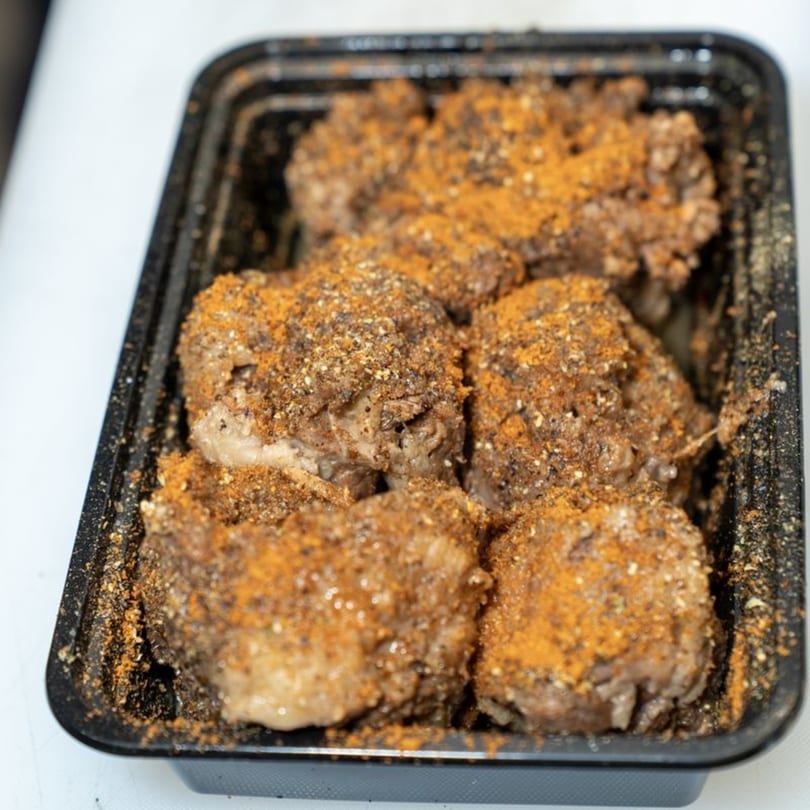 African suya meat, heavily spiced with orange and dark seasonings, in a black takeout container.