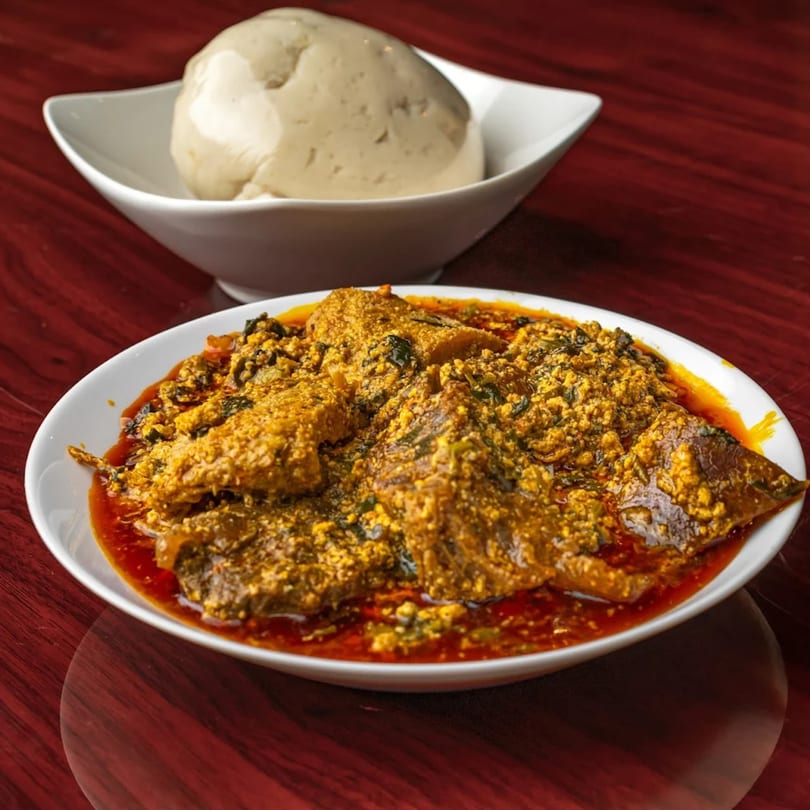 A bowl of Supreme Seafood & Suya's African egusi soup with fish and a side of fufu.