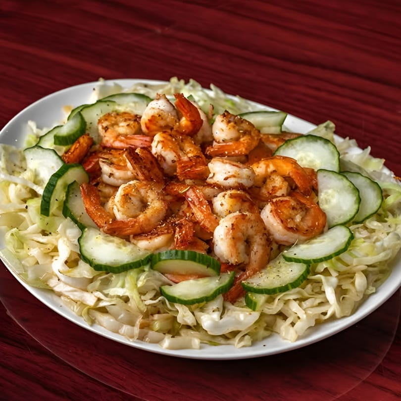 Grilled shrimp with sliced cucumbers and shredded cabbage on a white plate, Supreme Seafood & Suya.