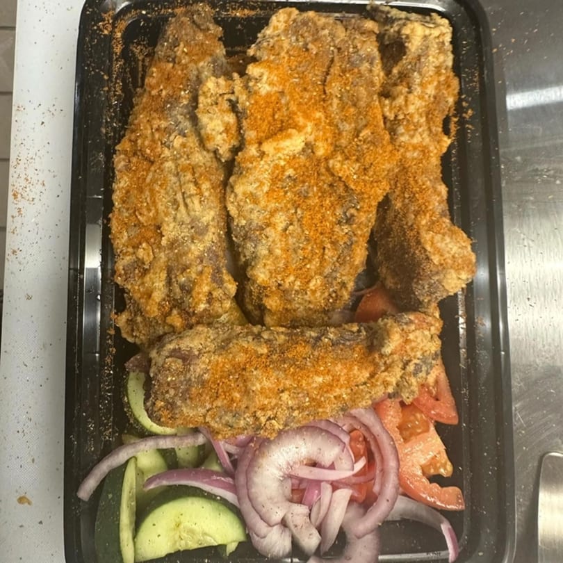 African suya meat with seasoning, served in a black container with sliced cucumbers, red onions, and tomatoes.