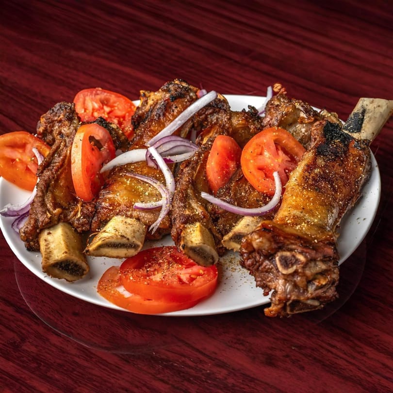 Grilled African beef ribs with sliced tomatoes and onions on a white plate.