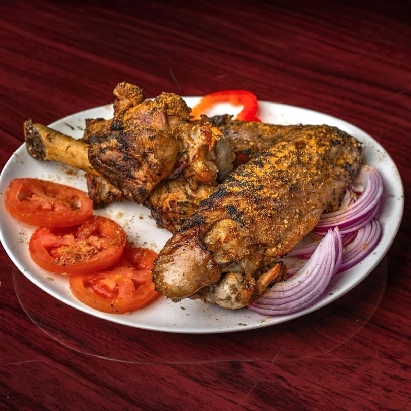 Grilled Supreme Seafood & Suya meat with spices, sliced tomatoes, and red onions on a white plate.