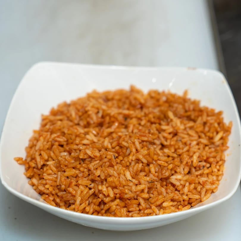 A white rectangular bowl filled with Supreme Seafood & Suya's African jollof rice.